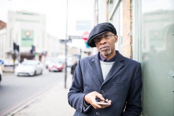 Man stood outside, leaning on a shop wall