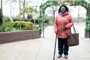 Woman stood outside in her coat leaning on a walking stick